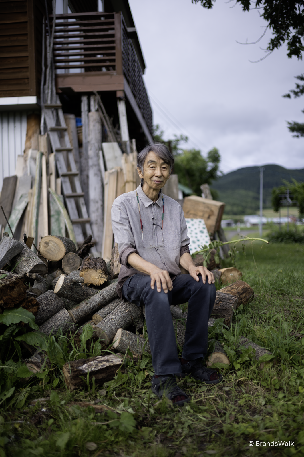 Tanno Norio seated on a pile of logs outside his home in Asahikawa