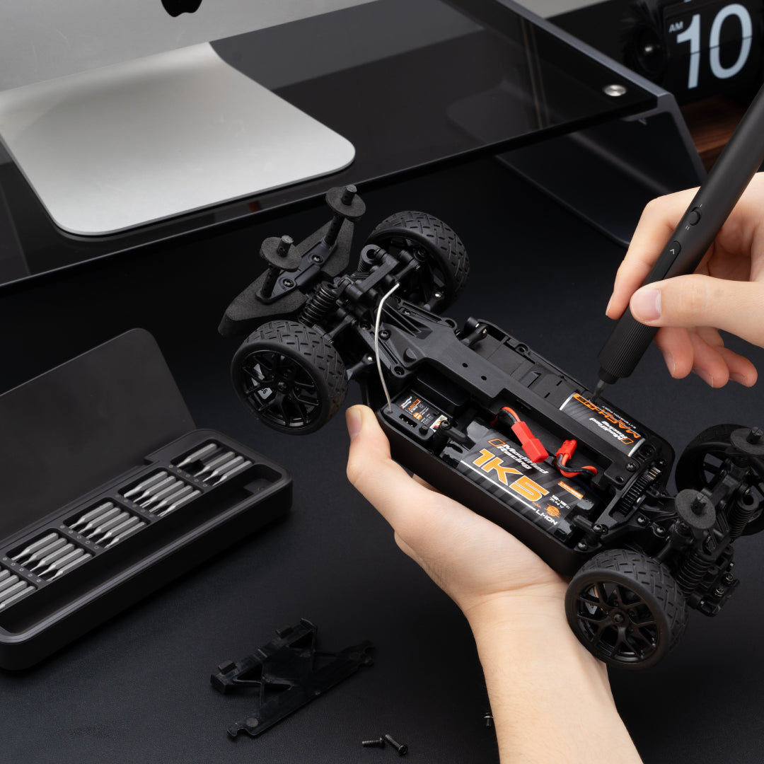 Person assembling a model car with tools on a black surface