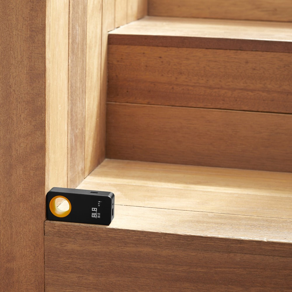 Black electronic device with a yellow light on a wooden surface, HOTO-Laser-Measure-display