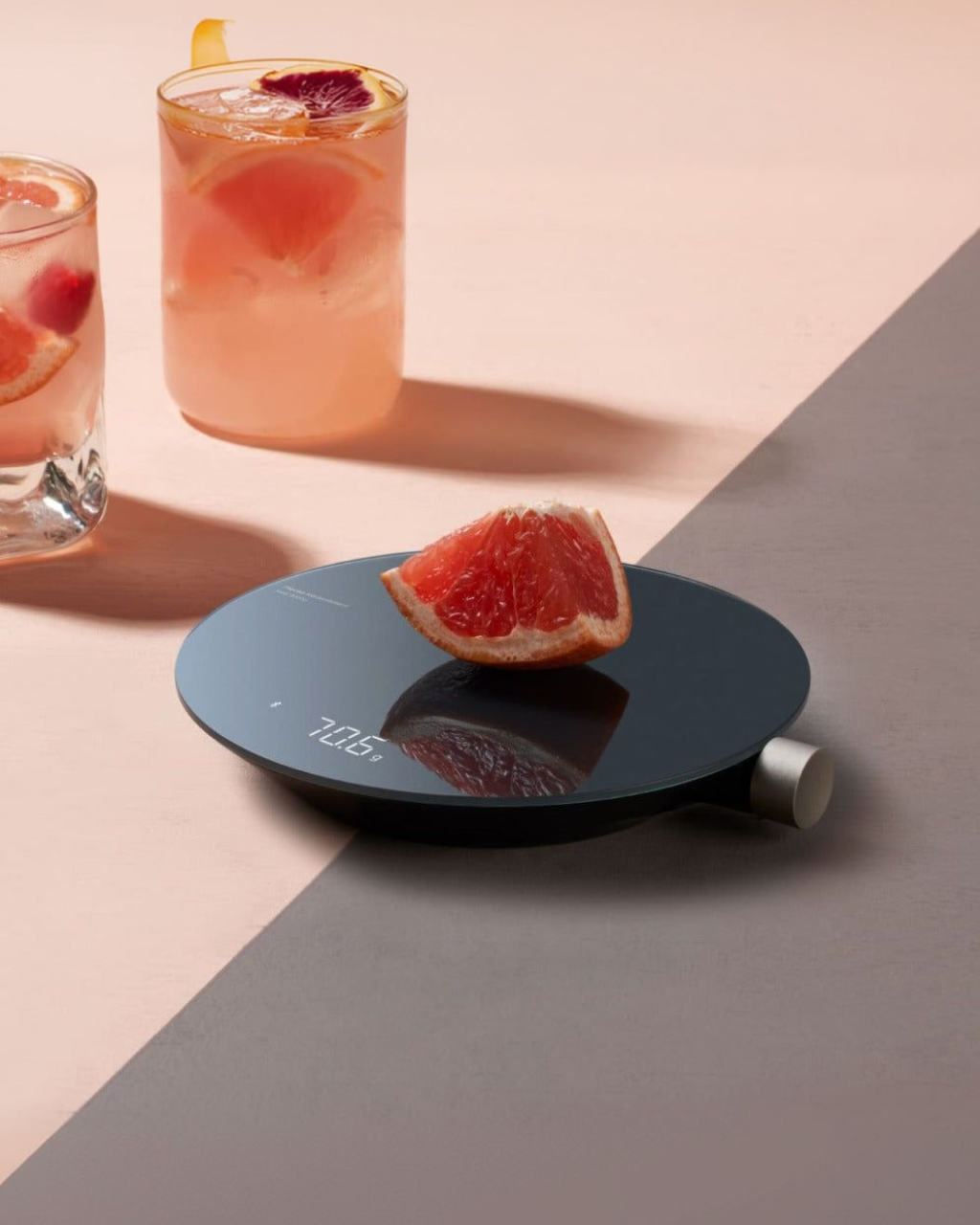 Digital kitchen scale with a grapefruit on a two-tone surface, with drinks in the background. HOTO Smart Kitchen Scale