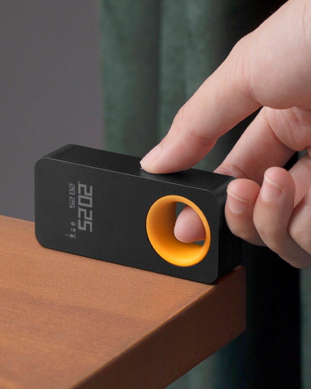 Hand interacting with a black and orange device on a wooden surface, HOTO Laser Measure