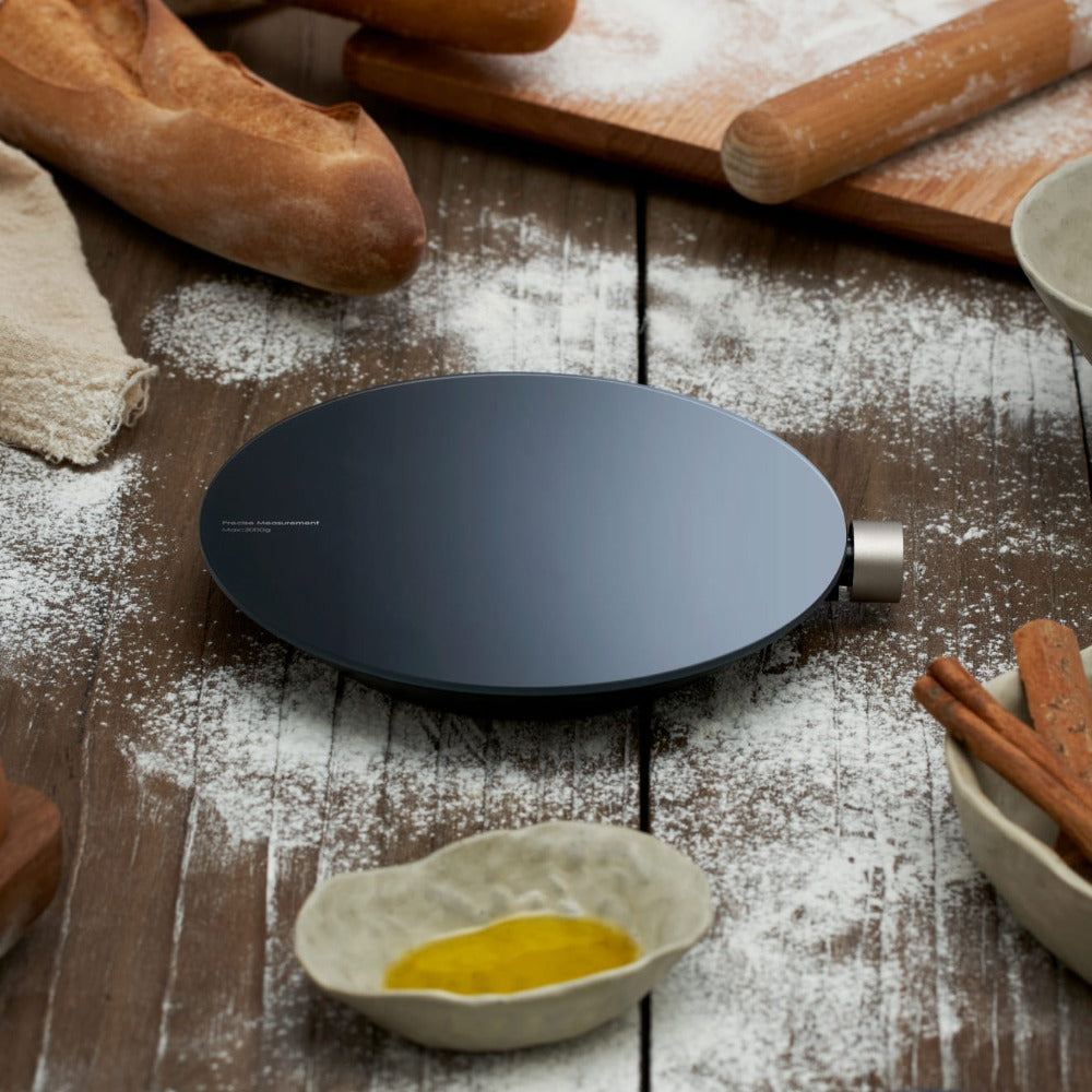 Black round appliance on a wooden surface with bread, rolling pin, and flour. HOTO Smart Kitchen Scale