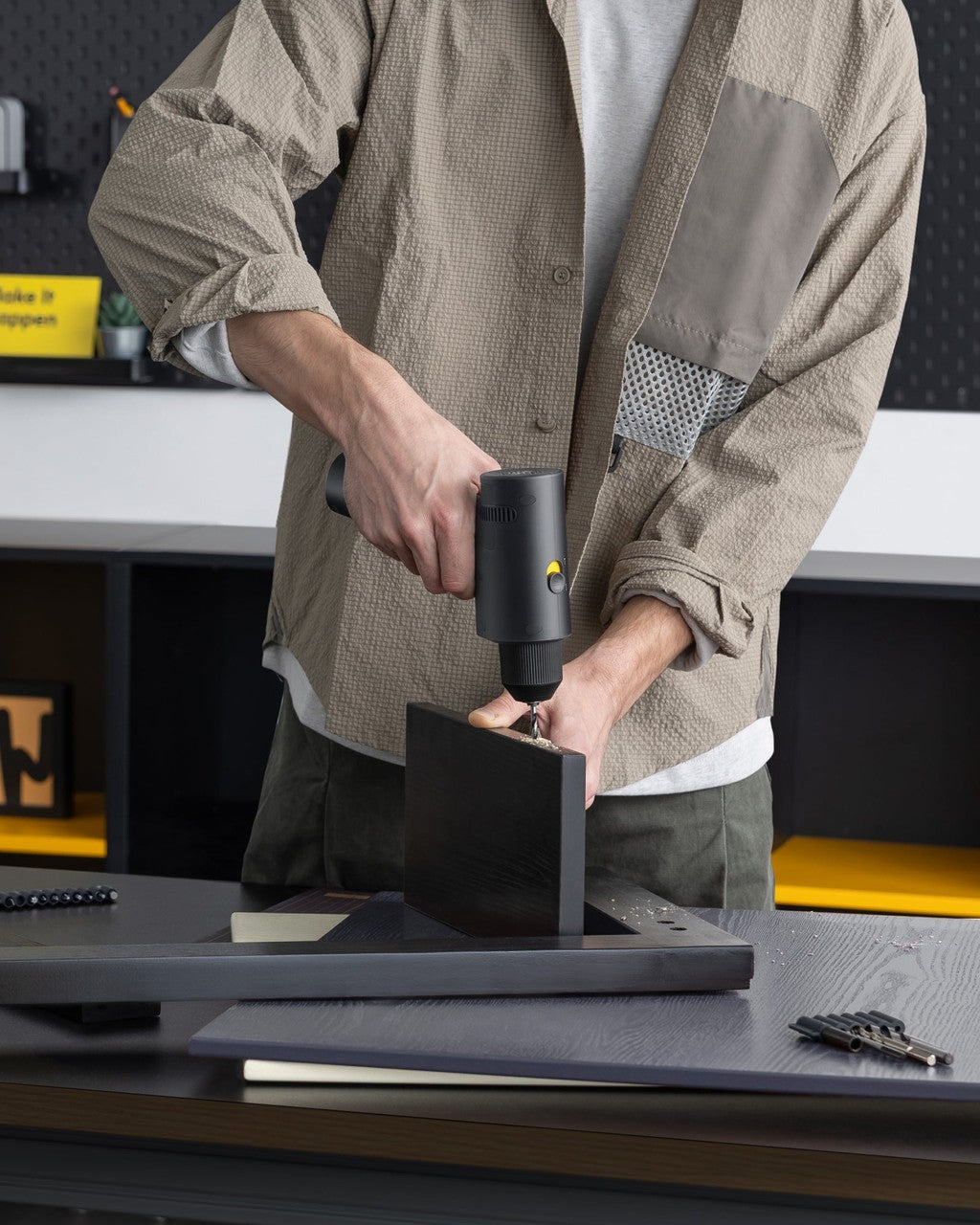 Person using a black tool on a metal object in a workshop setting