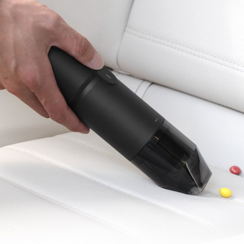 Hand using a black handheld vacuum cleaner on a white car seat.