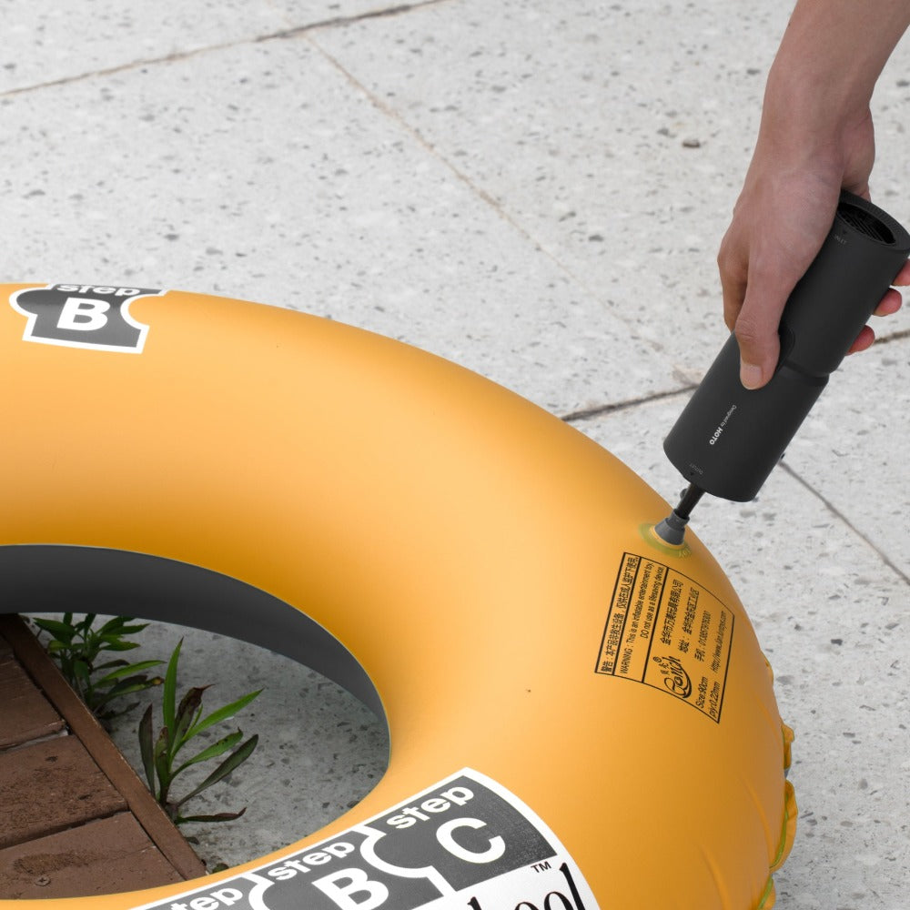 Person inflating a yellow inner tube with a hand pump on a concrete surface.