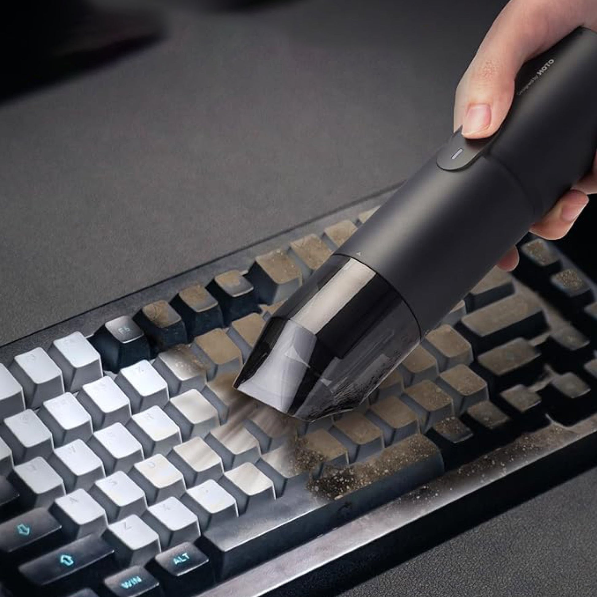 Hand using a black handheld vacuum cleaner to clean a keyboard HOTO Compressed Air Capsule