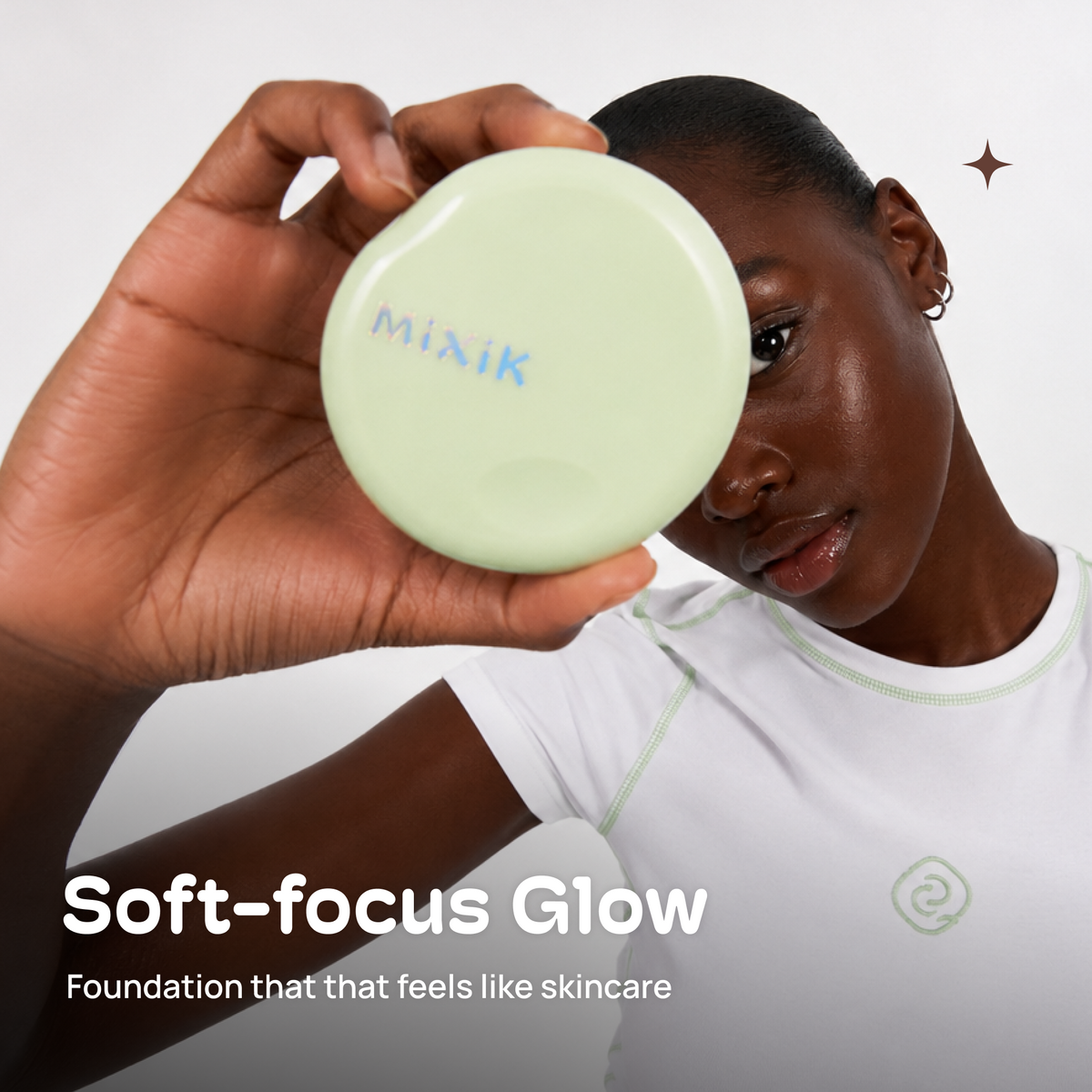 A person holds a round pale green foundation compact labeled 'MIXIK' toward the camera. The person is wearing a white athletic-style top with a small green swirl logo. MIXIK Cloud Cover Soothing Cushion | Espresso Deep