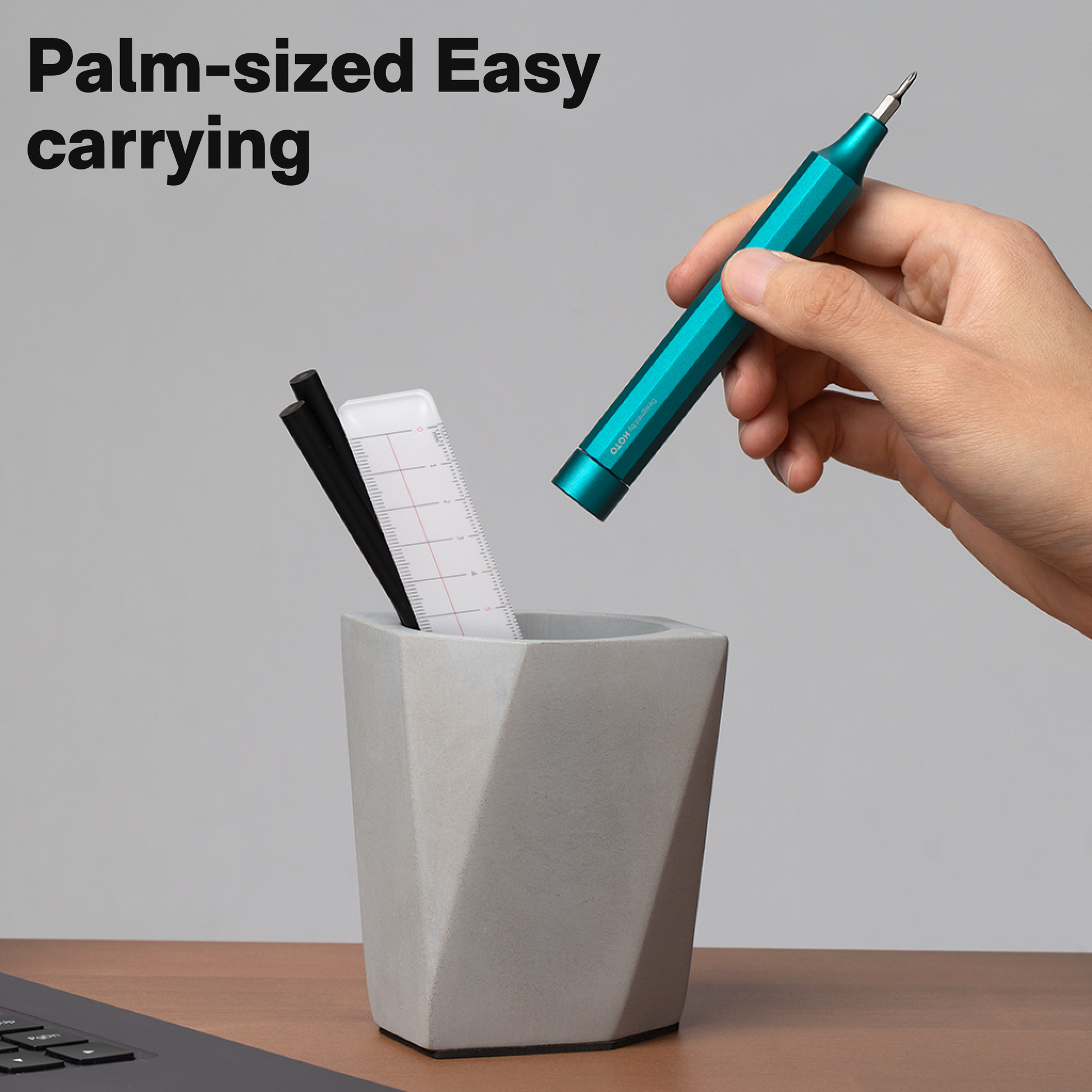 Hand holding a teal pen over a geometric gray pen holder with text 'Palm-sized Easy carrying'. HOTO Precision Manual Screwdriver Pen | Azure Blue