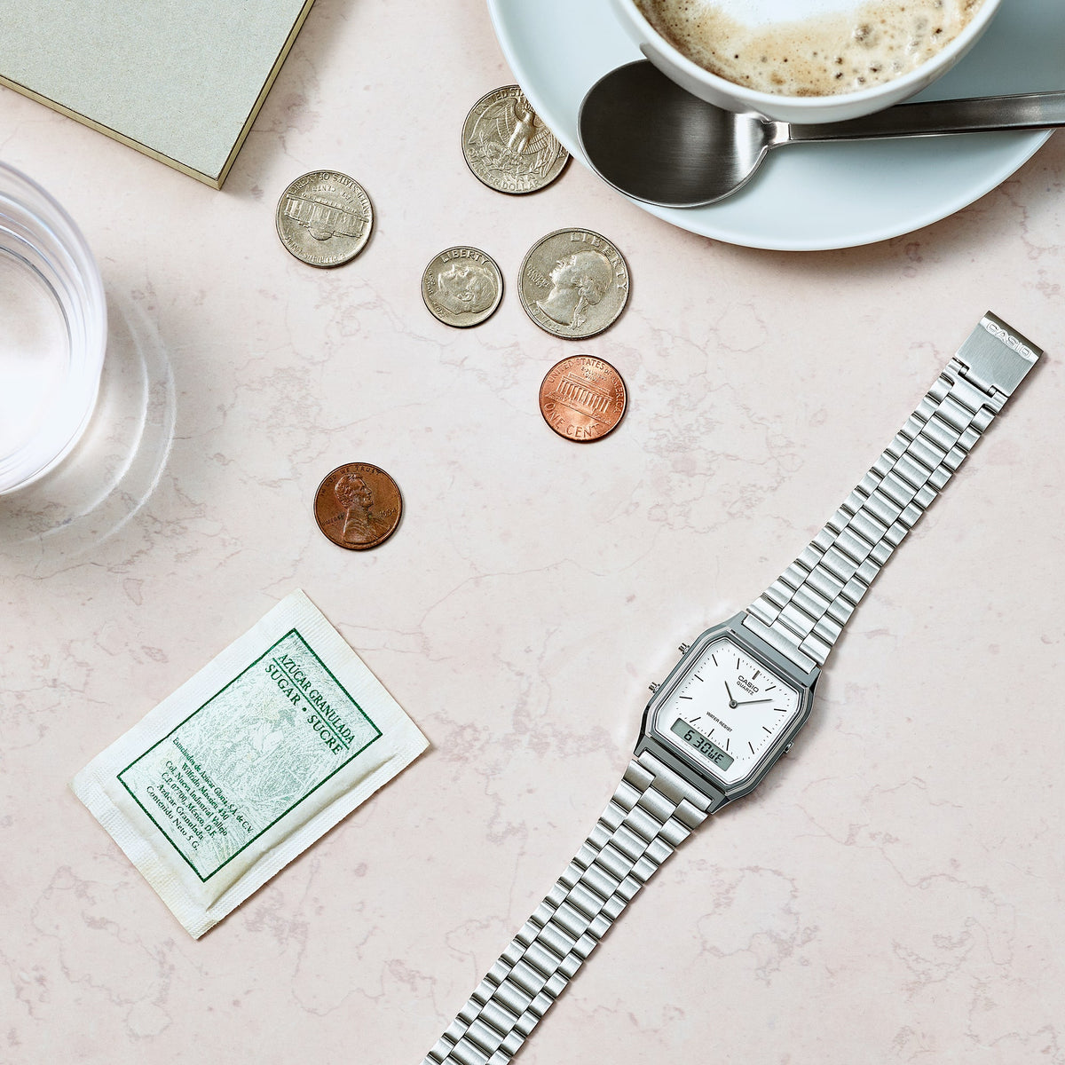 Casio AQ230A-7DM silver watch beside a coffee cup and travel items