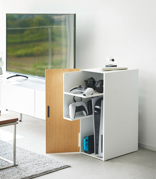 Yamazaki Home Tower Video Game Storage Cabinet - Steel — open white cabinet storing consoles and controllers beside a TV.