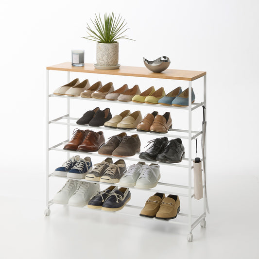 White five-tier rolling shoe rack filled with shoes, with a wood top displaying a plant, candle and bowl; styling items not included.