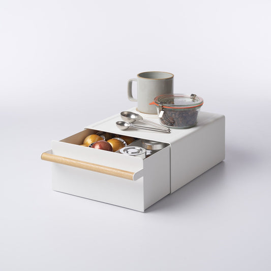 Yamazaki Tosca white countertop rack with a wood drawer handle, shown with the drawer open beneath a mug, jar and measuring spoons; contents not included.