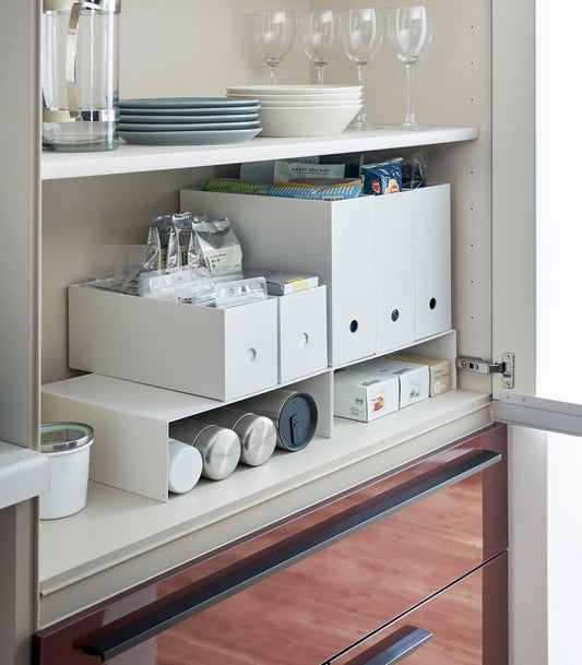 Yamazaki Home Tower Steel Riser Shelves - Set of 2, white risers holding storage boxes above bottles inside cabinet