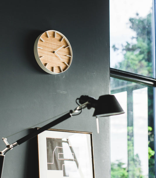 Yamazaki Home Rin Wall Clock - Steel + Wood, Ash clock on dark wall beside a window