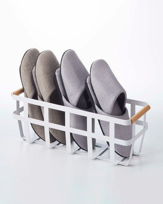 White Yamazaki Tosca small storage basket with wood handles, shown holding two pairs of separate slippers.