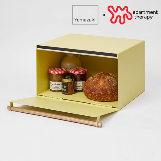 Yamazaki Home Bread Box - Yellow Pear Steel and Wood — open Yellow Pear box with bread and jars, showing Yamazaki x Apartment Therapy collaboration logos.