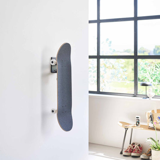 Yamazaki Tower black wall-mounted skateboard holder displaying a skateboard vertically beside a window; skateboard not included.