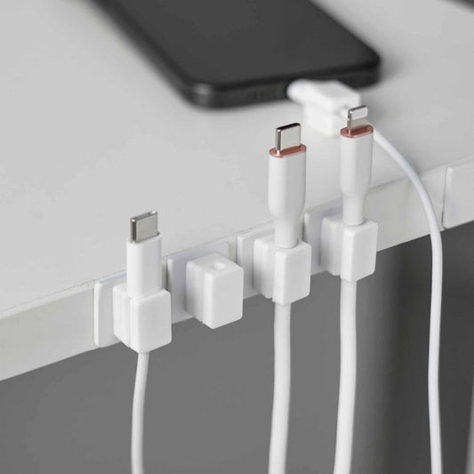 White magnetic cable holders and bases along a desk edge with separate charging cables and phone