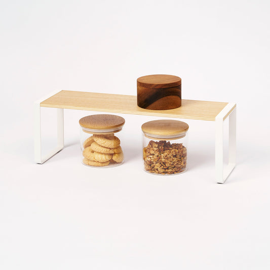 Yamazaki Home Tosca Single-Tier Riser - Steel + Wood, wood shelf holding a box above glass storage jars