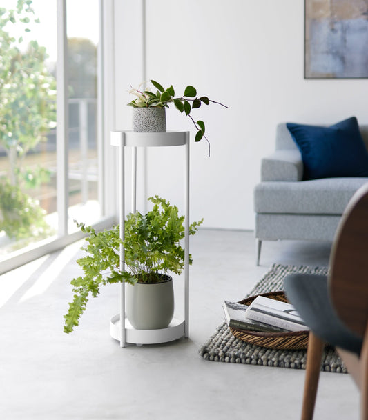 Yamazaki Home Tower Two-Tier Indoor Rolling Plant Stand, white stand holding two plants beside window