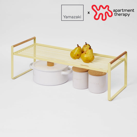 Yamazaki Home Countertop Wire Shelf - Yellow Pear — Yellow Pear shelf with pears and cookware, showing Yamazaki x Apartment Therapy collaboration logos.