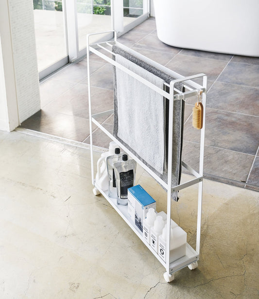 Yamazaki Home Tower Rolling Towel Rack (33 in) - Steel, white rack holding towels and toiletries beside bathtub