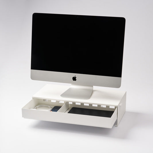 Yamazaki Tower white monitor stand with its drawer open beneath a desktop computer, showing stored cables and small items; electronics not included.