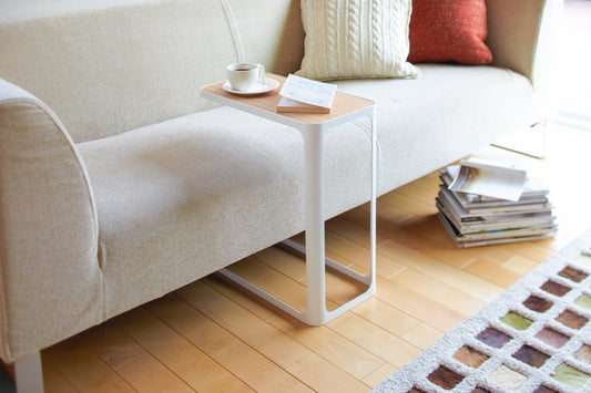 Yamazaki Home Frame C Side Table (20" H) - Steel, white C-shaped table with cup and book over a sofa seat